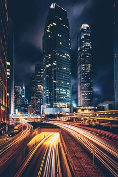 Street traffic in Hong Kong at night. Office skyscraper buildings and busy traffic on highway road with blurred cars light trails. Hong Kong, China