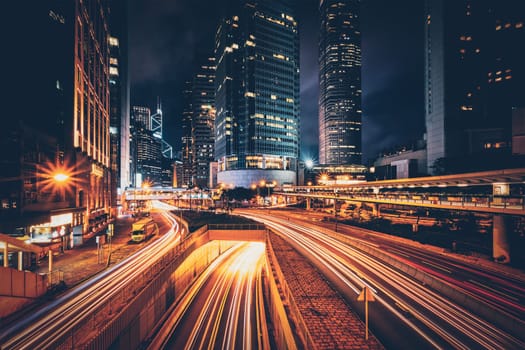 Street traffic in Hong Kong at night. Office skyscraper buildings and busy traffic on highway road with blurred cars light trails. Hong Kong, China