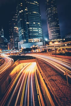 Street traffic in Hong Kong at night. Office skyscraper buildings and busy traffic on highway road with blurred cars light trails. Hong Kong, China