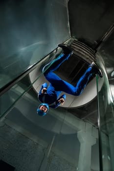 A man in overalls and a protective helmet enjoys flying in a wind tunnel. Free fall simulator.