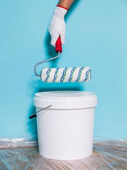 Image of paint can and man holding paint roller in front of blue wall.