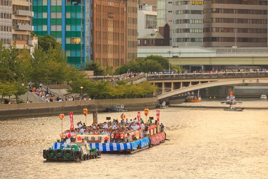 Osaka, Japan - July 25, 2023: Tug boat pulls crowded barge down river at Tenjin Matsuri. High quality photo