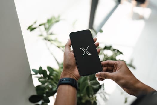 CHIANG MAI, THAILAND- JULY 26, 2023 : Man using iPhone open Twitter application showing X new logo, online social networking and service that enables users to send and read messages..