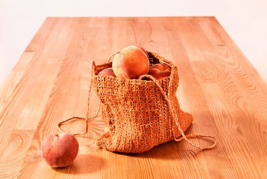 Ripe fruit of peaches in orange shopping bag on wooden table , 