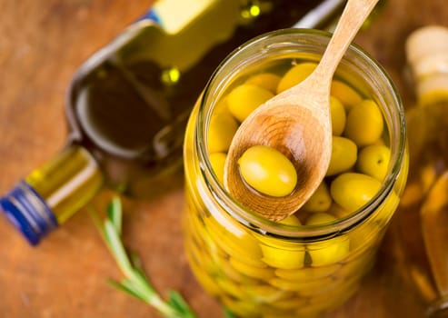 Close up green olives in bank, rosemary on a wooden background