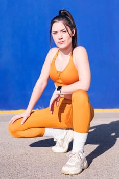 vertical photo of a sportswoman squatting while posing on the street in a blue background, concept of sport and healthy lifestyle, copy space for text