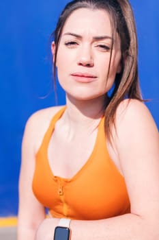 vertical close up portrait of a confident caucasian sportswoman looking at camera in a blue background, concept of real people and sporty lifestyle