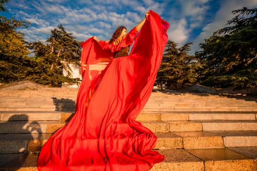 Sunrise red dress. A woman in a long red dress against the backdrop of sunrise, bright golden light of the sun's rays. The concept of femininity, harmony