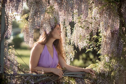 Woman wisteria lilac dress. Thoughtful happy mature woman in purple dress surrounded by chinese wisteria.