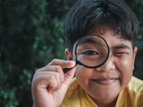 Front view portrait of a young asian child holding a magnifying glass for reading in hand inspecting. Investigating to have close look with eye in focus.