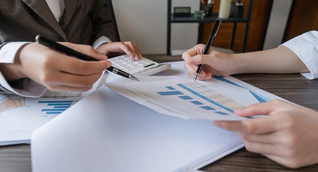 Two Asian business women Discussing Financial reports, analytical concepts, planning and financial statistics and investment markets at the office.