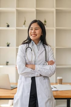 Beautiful young asian doctor standing smiling with crossed arms and stethoscope in office at hospital.