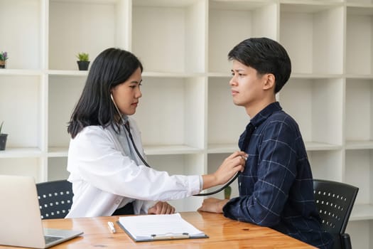 Asian man patient are checked up his health while a woman doctor use a stethoscope to hear heart rate of him.