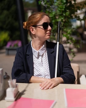 A blind woman in a business suit is sitting in an outdoor cafe