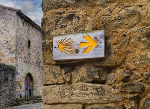 Wooden board on a stone wall with the indication of the Camino de Santiago in the Cantabrian town of Santillana del Mar.