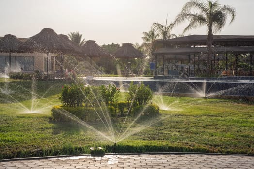 Panoramic landscape view of rural countryside public park outdoor area with water sprinklers on in tropical ornamental garden