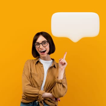 I have an idea. Emotional lady wearing eyeglasses having great thought, finding inspiration or solution to problem, pointing finger up, showing blank communication bubble, posing on yellow background