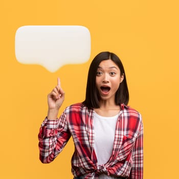 Great idea, inspiration concept. Emotional young asian lady have wow creative idea, raising finger up at communication bubble with blank space and looking at camera with open mouth, yellow background