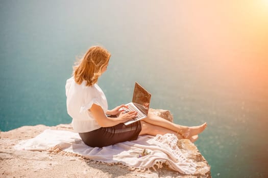 Freelance woman working on a laptop by the sea, typing away on the keyboard while enjoying the beautiful view, highlighting the idea of remote work