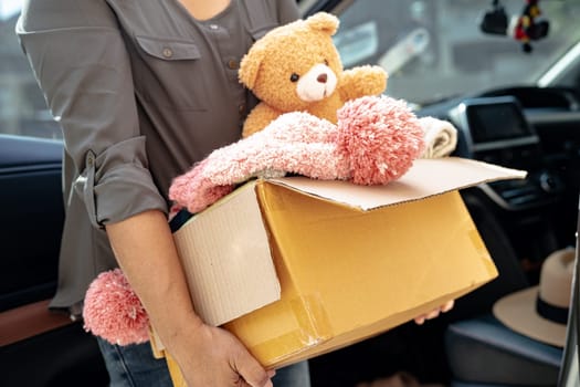 Volunteer woman provide clothing donation box with used clothes and doll in car to support help for refugee, homeless or poor people in the world.