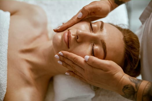 Therapist is doing face relaxing massage to a young woman in modern wellness cabinet