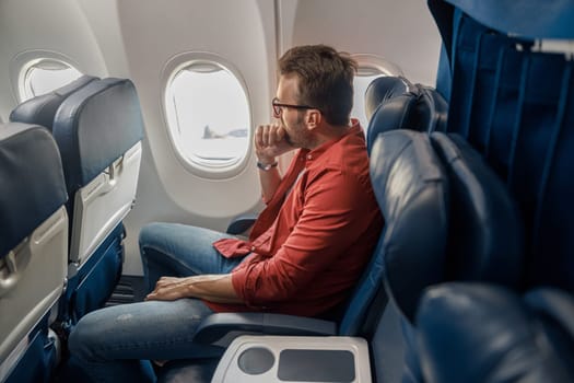Pensive caucasian man in casual wear resting on the plane, sitting and looking out the window. Relax, travel, vacation, transportation concept