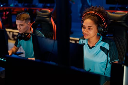 Photo of focused African female cybersport gamer wearing headphones playing online video games in contemporary e-sports club