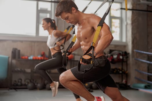 Athletic man in training gloves with young lady exercising on stretching tapes in the fitness club