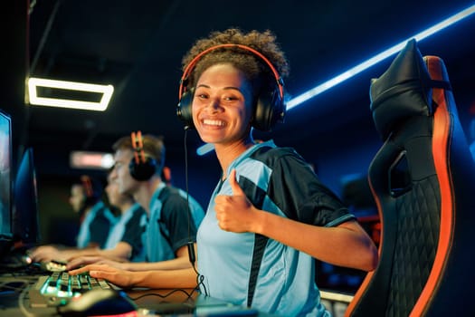 Happy female gamer showing thumb up sign and smiling while using powerful computer for online game in computer club