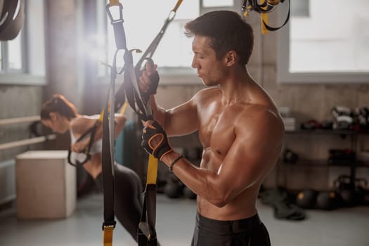 Young muscular man in workout gloves holding stretching tape and getting ready for training in the fitness club