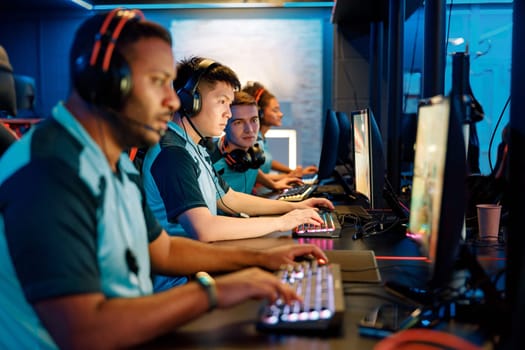 Group of multi-ethnic cybersport players in headsets sitting in front of computers and playing video games online in computer club