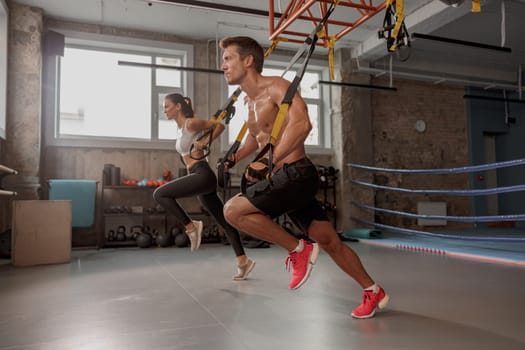 Strong man in training gloves with slender female doing stretching exercises in the gym and looking ahead