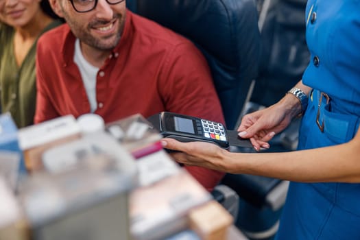 Close up shot of airline stewardess holding terminal while cheerful male passenger making payment. Travel, service, transportation, airplane concept