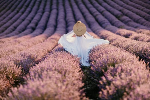 Happy woman in a white dress and straw hat strolling through a lavender field at sunrise, taking in the tranquil atmosphere