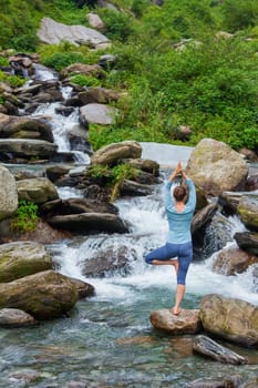 Woman in Hatha yoga balance yoga asana Vrikshasana tree pose at waterfall outdoors