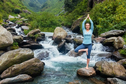 Woman in Hatha yoga balance yoga asana Vrikshasana tree pose at waterfall outdoors