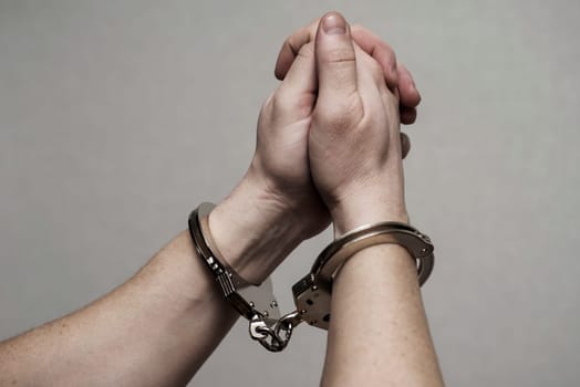 Handcuff on mans arms, praying for forgiveness. Chained hands praying. Praying inmate.
