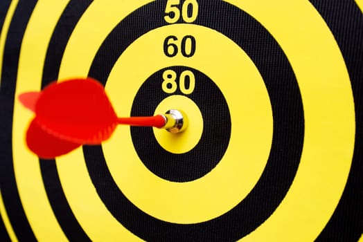 Closeup of a dartboard with yellow and red magnetic darts. Dart in bulls eye of dartboard concept for hitting target dart success concept.