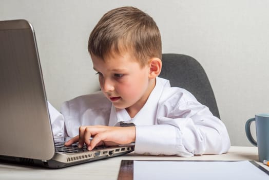 Little boss in the office. A kid businessman with glasses with laptop working in office.