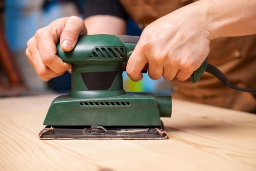 Closeup of carpenter sanding wooden planks with electrical sanding machine. A carpenter grinds wood with sander machine.