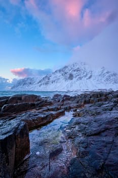 Beach of Norwegian sea on rocky coast in fjord on sunset in winter. Vareid beach, Lofoten islands, Norway