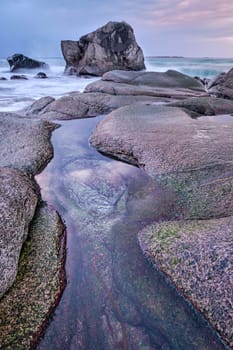 Rocks on beach of fjord of Norwegian sea in winteron sunset. Utakliev beach, Lofoten islands, Norway