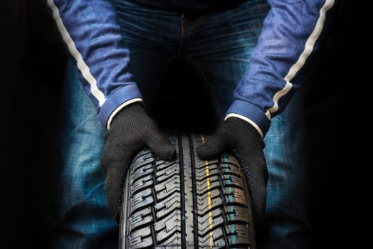 Hands of a mechanic in gloves hold a tire. Automobile mechanic with car tire. Car wheel replacement.