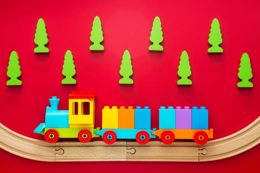 Colorful toy train on wooden railway with green trees on red background. Kids background.