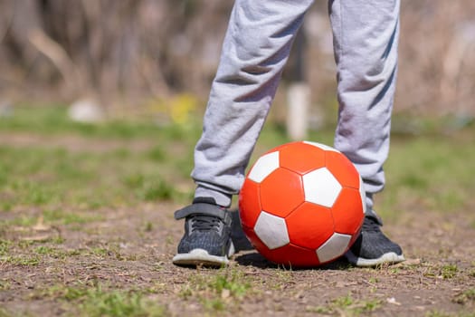 Close up view of boy's legs and ball on football field in the park. Kids activities.