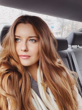 Young woman with long hair, wavy hairstyle in the car or taxi cab as passenger, exploring the city, transport and travel idea