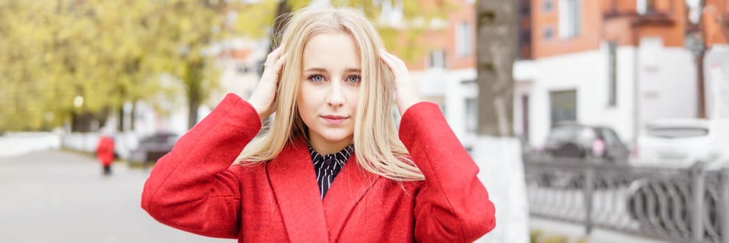 A young blonde woman walks around the autumn city in a red coat. The concept of urban style and lifestyle.