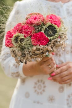 The bride holds her wedding bouquet with red peonies and sunflowers in her hands.