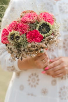 The bride holds her wedding bouquet with red peonies and sunflowers in her hands.