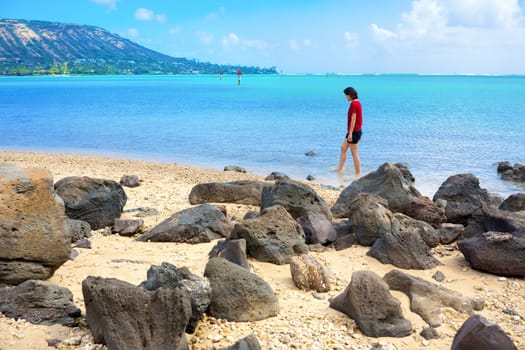 Young woman walking alone on rocky Hawaiian beach with Kokohead Crater in background